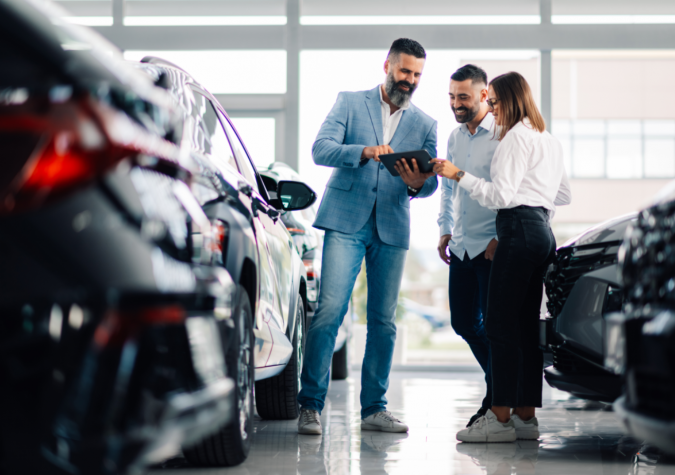 A car salesman showing buyers a tablet as they explore the dealership showroom